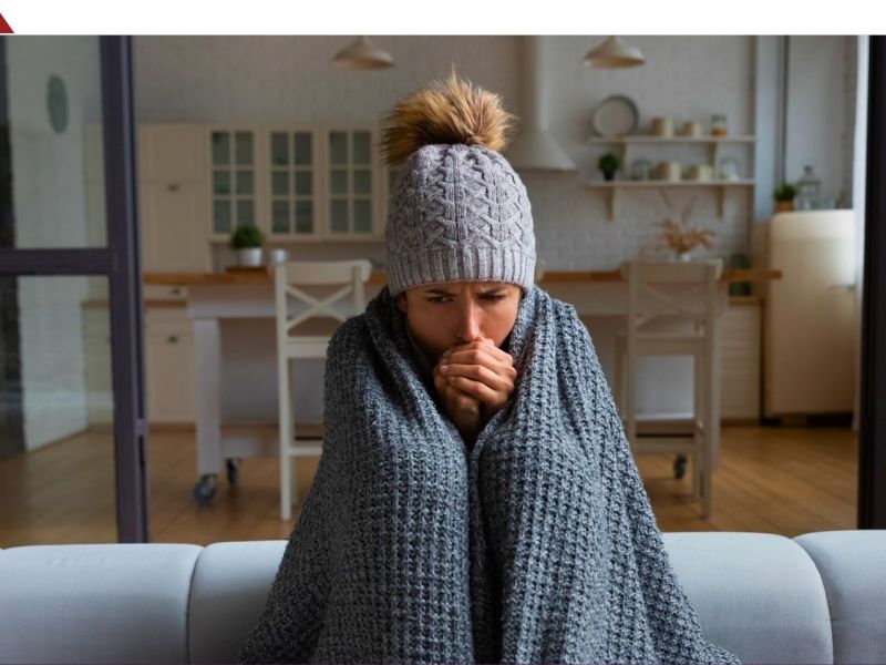 Frau sitzt in eine Decke gehüllt auf einem Sofa