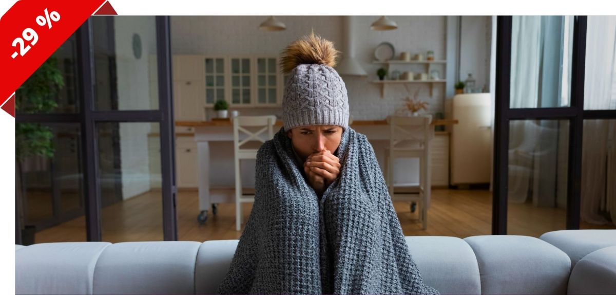 Frau sitzt in eine Decke gehüllt auf einem Sofa