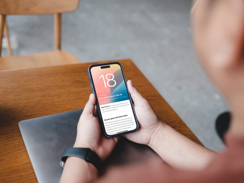 Person hält ein iPhone in der Hand, auf dem iOS 18 geladen ist.