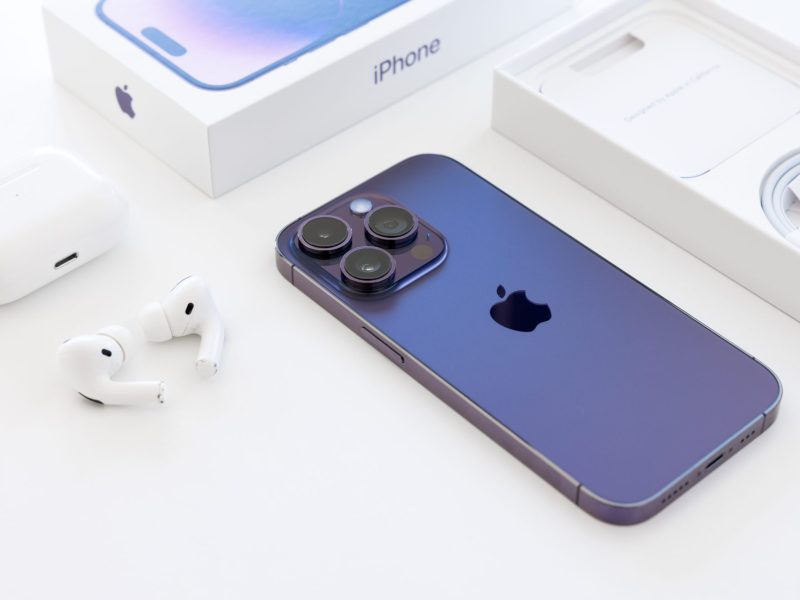 iPhone liegt neben einer Verpackung und Kopfhörer auf einem weißen Untergrund.