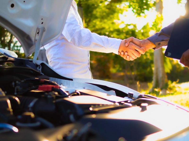 Auto mit offener Motorhaube vor zwei Personen, die sich die Hand schütteln