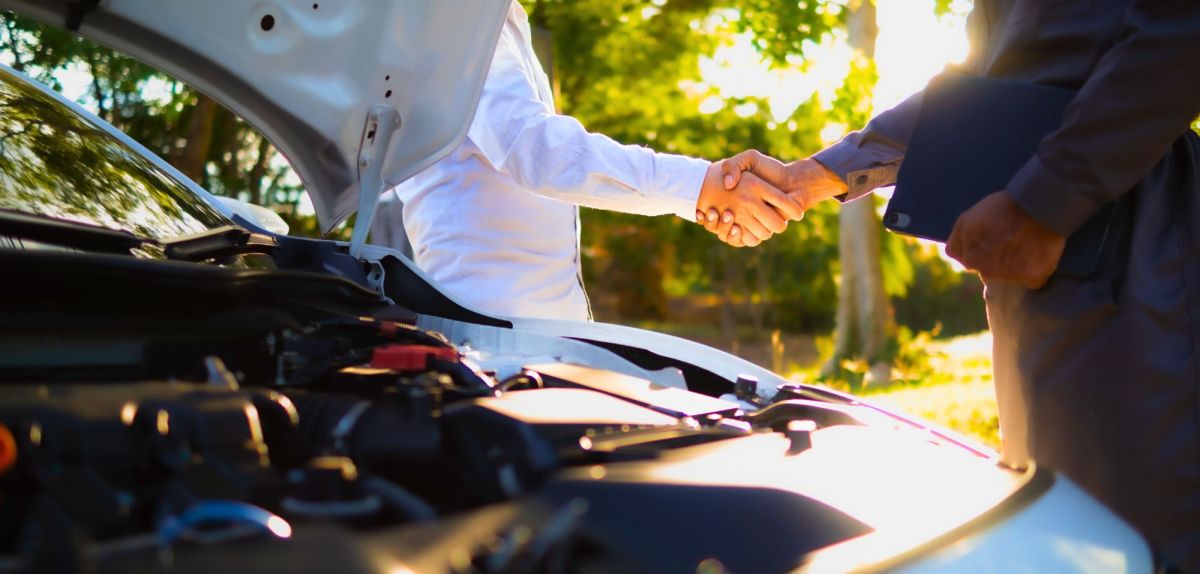Auto mit offener Motorhaube vor zwei Personen, die sich die Hand schütteln