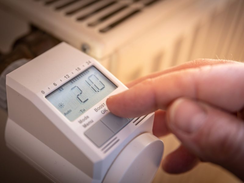 Person stellt smartes Thermostat an einem Heizkörper ein.