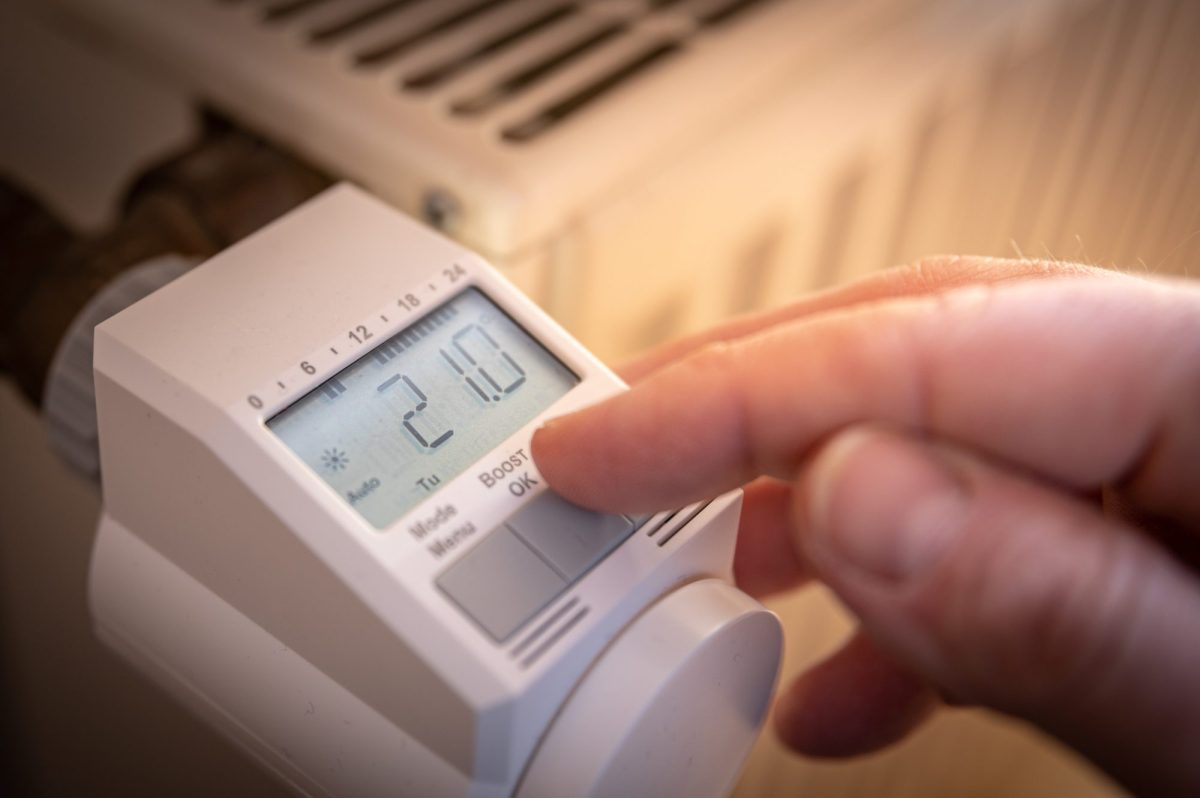Person stellt smartes Thermostat an einem Heizkörper ein.