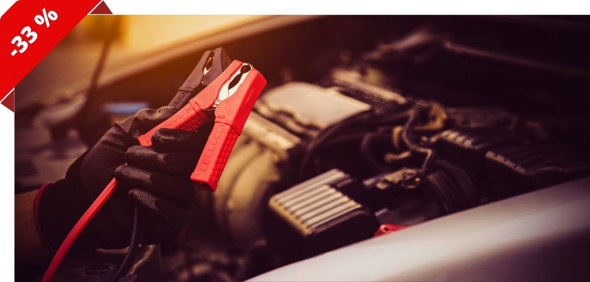 Person hält zwei Starthilfekabel über den Motorraum eines Autos
