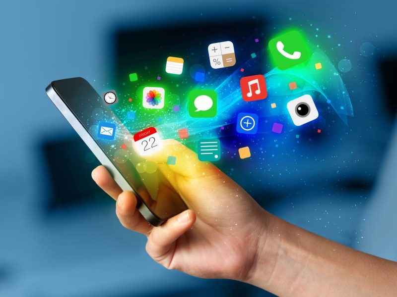 Person hält ein Handy in der Hand. Davor werden mehrere App-Symbole angezeigt.