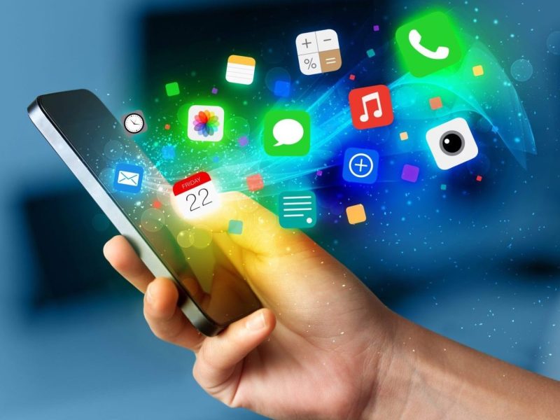 Person hält ein Handy in der Hand. Davor werden mehrere App-Symbole angezeigt.