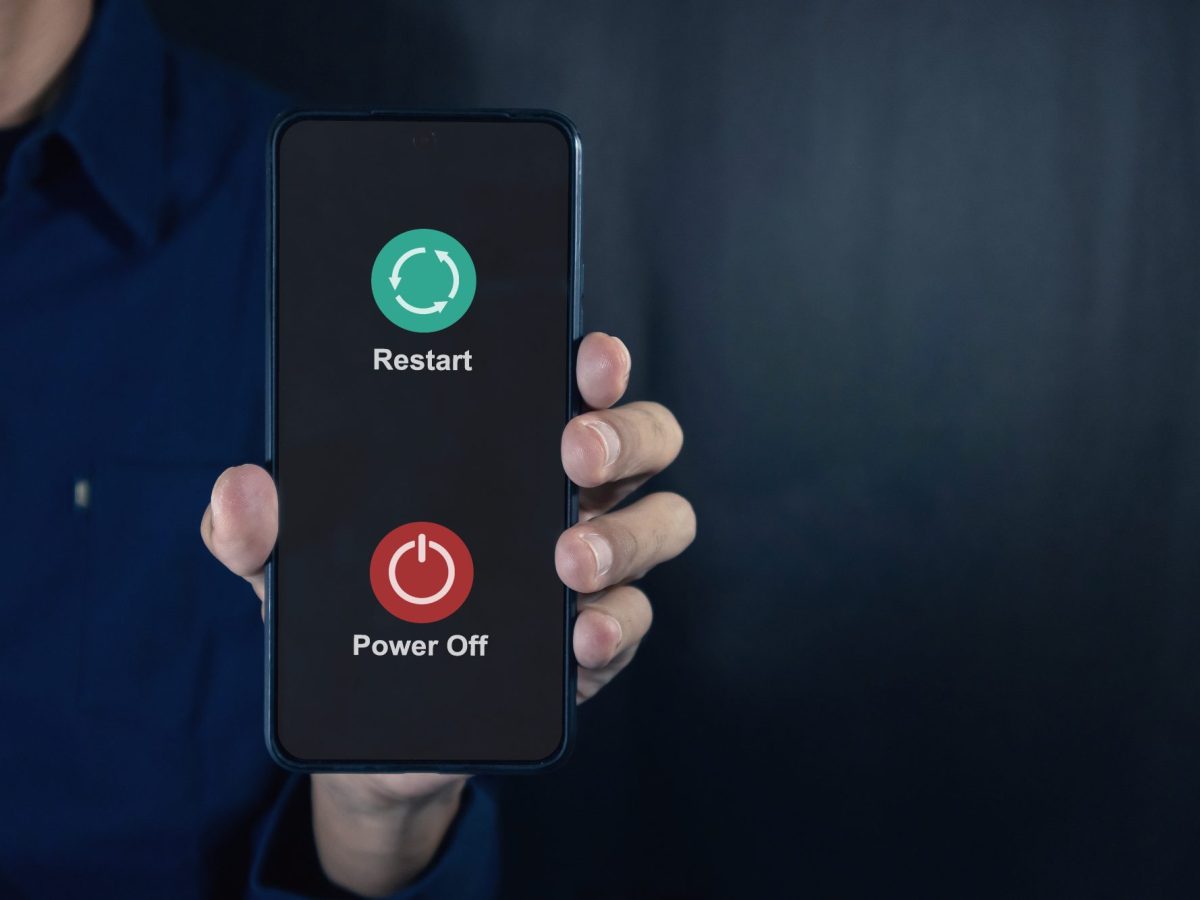 Eine Person hält ein Handy in der Hand. Auf dessen Display werden die Optionen angezeigt, das Handy auszuschalten oder neu zu starten.