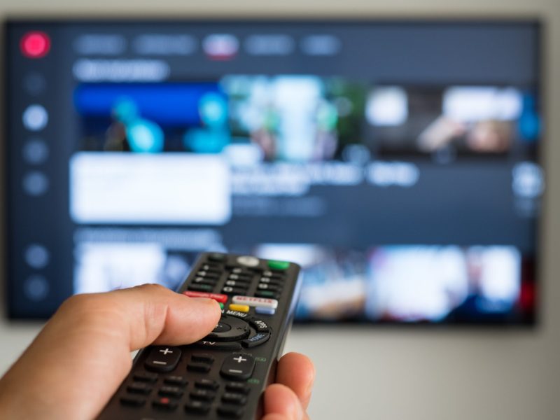 Person hält eine Fernbedienung auf einen Fernseher gerichtet.