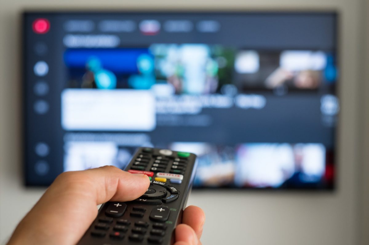 Person hält eine Fernbedienung auf einen Fernseher gerichtet.