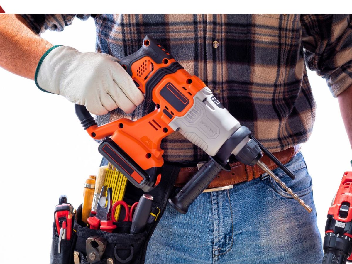 Eine Person mit Werkzeuggürtel hält einen Akku-Bohrhammer in der Hand.