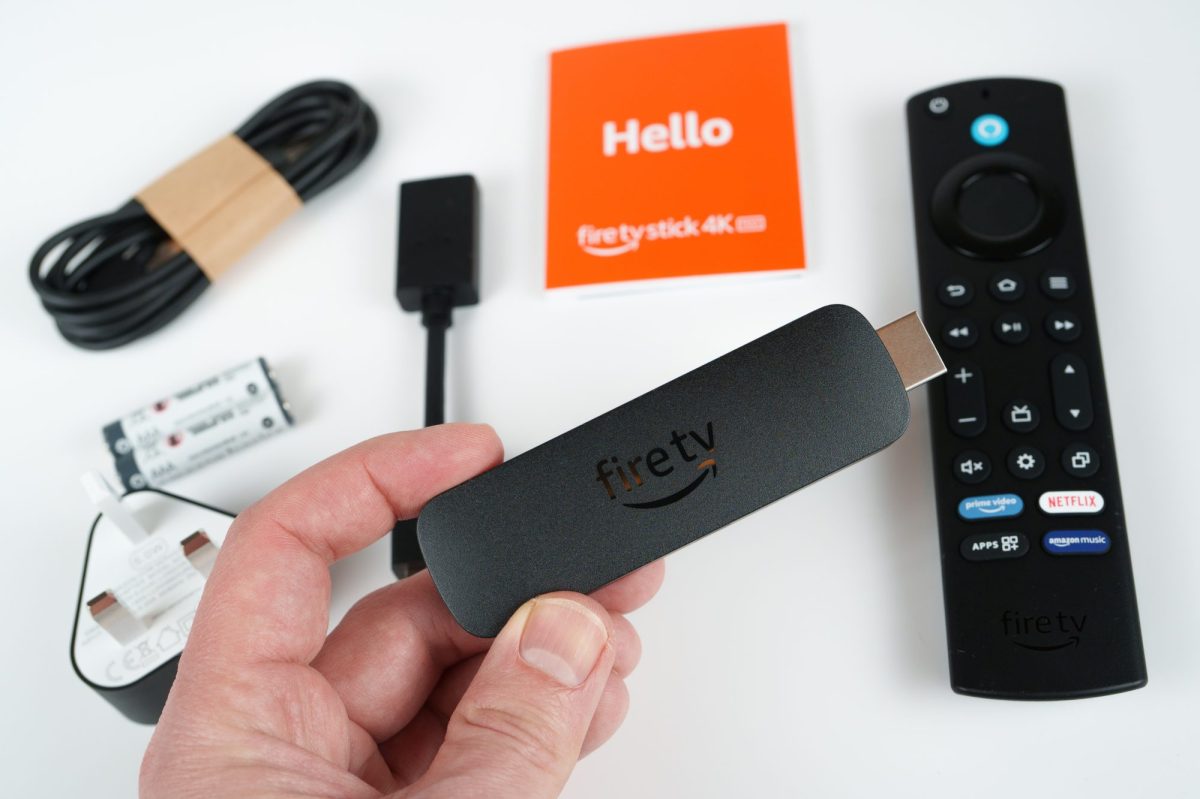 Person hält einen Amazon Fire TV-Stick. IM Hintergrund liegt das entsprechende Zubehör.