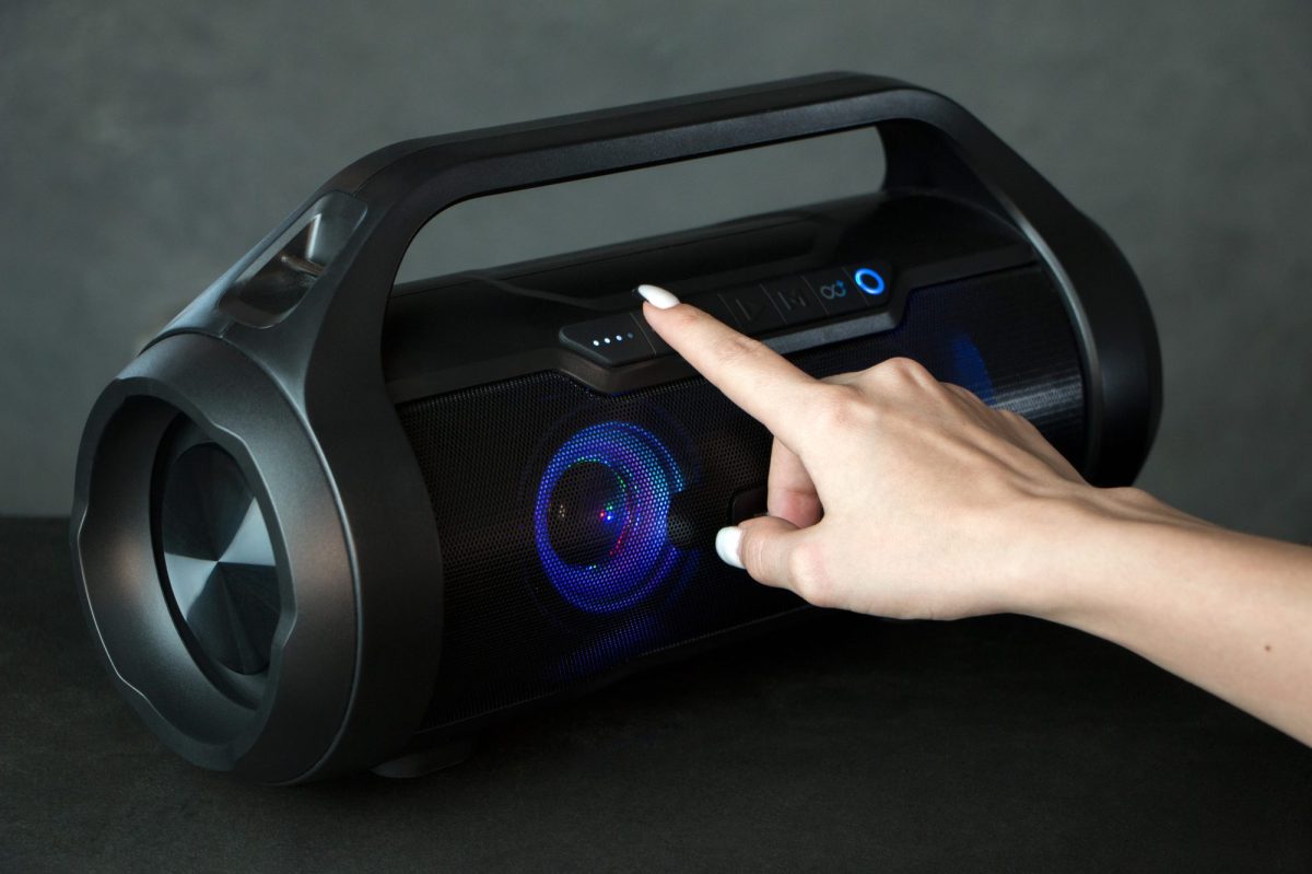 Person drückt auf eine Taste eines Bluetooth-Laustprechers.