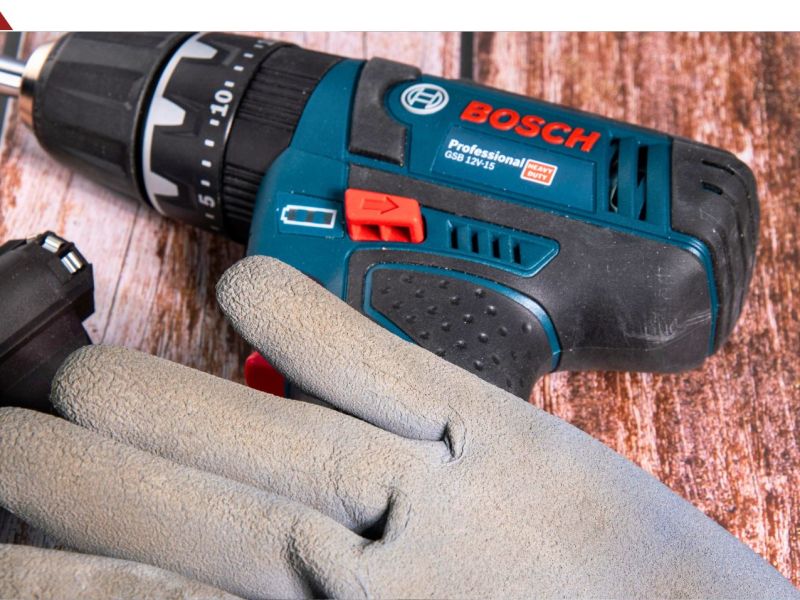 Bosch-Akkubohrschrauber liegt auf einem Untergrund aus Holz. Davor liegt ein Schutzhandschuh.