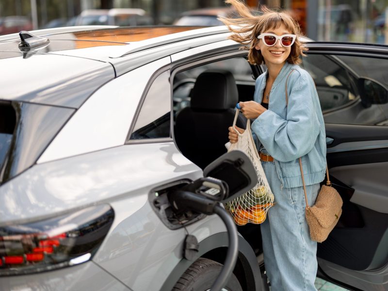 Frau lädt ihre Einkäufe in ein Elektroauto, das an eine Ladesäule angeschlossen ist.