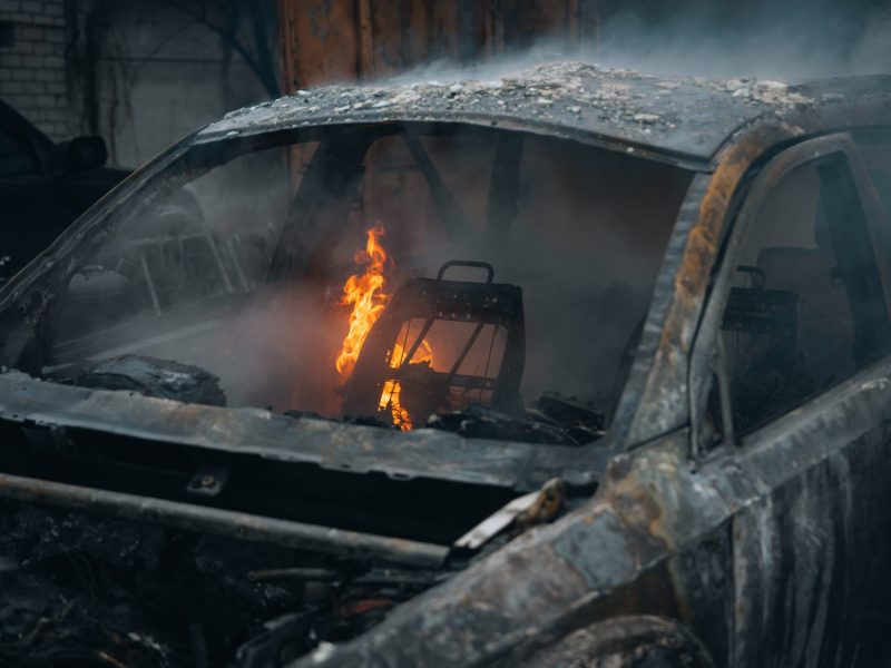 Ausgebranntes Auto. Im Inneren lodert noch eine Flamme.