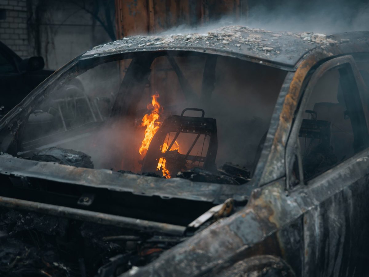 Ausgebranntes Auto. Im Inneren lodert noch eine Flamme.