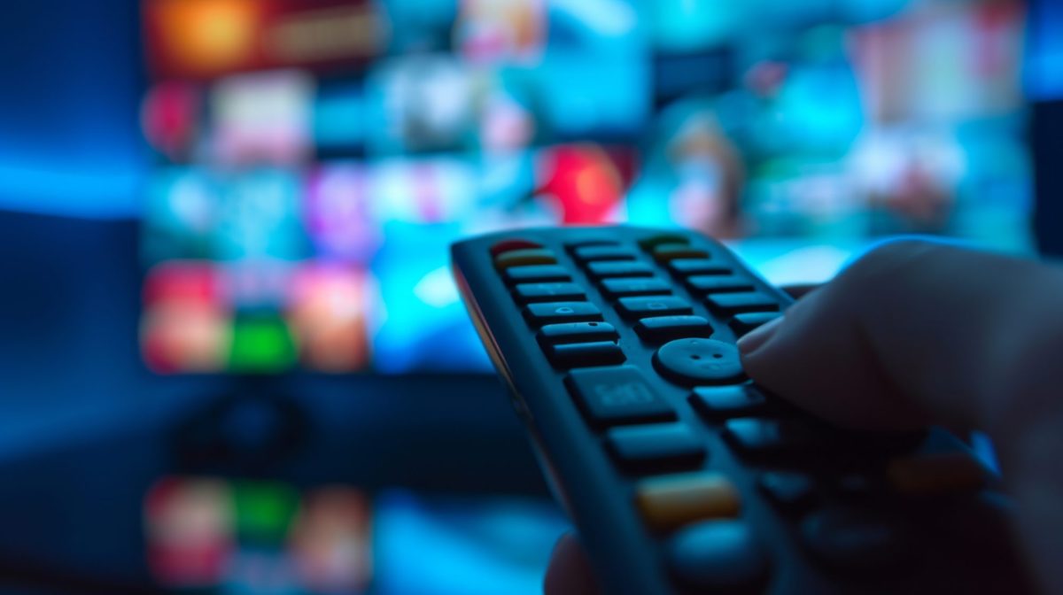 KI-generiertes BIld einer Hand, die eine Fernbedienung hält. Im Hintergrund ist ein eingeschalteter Fernseher zu sehen.
