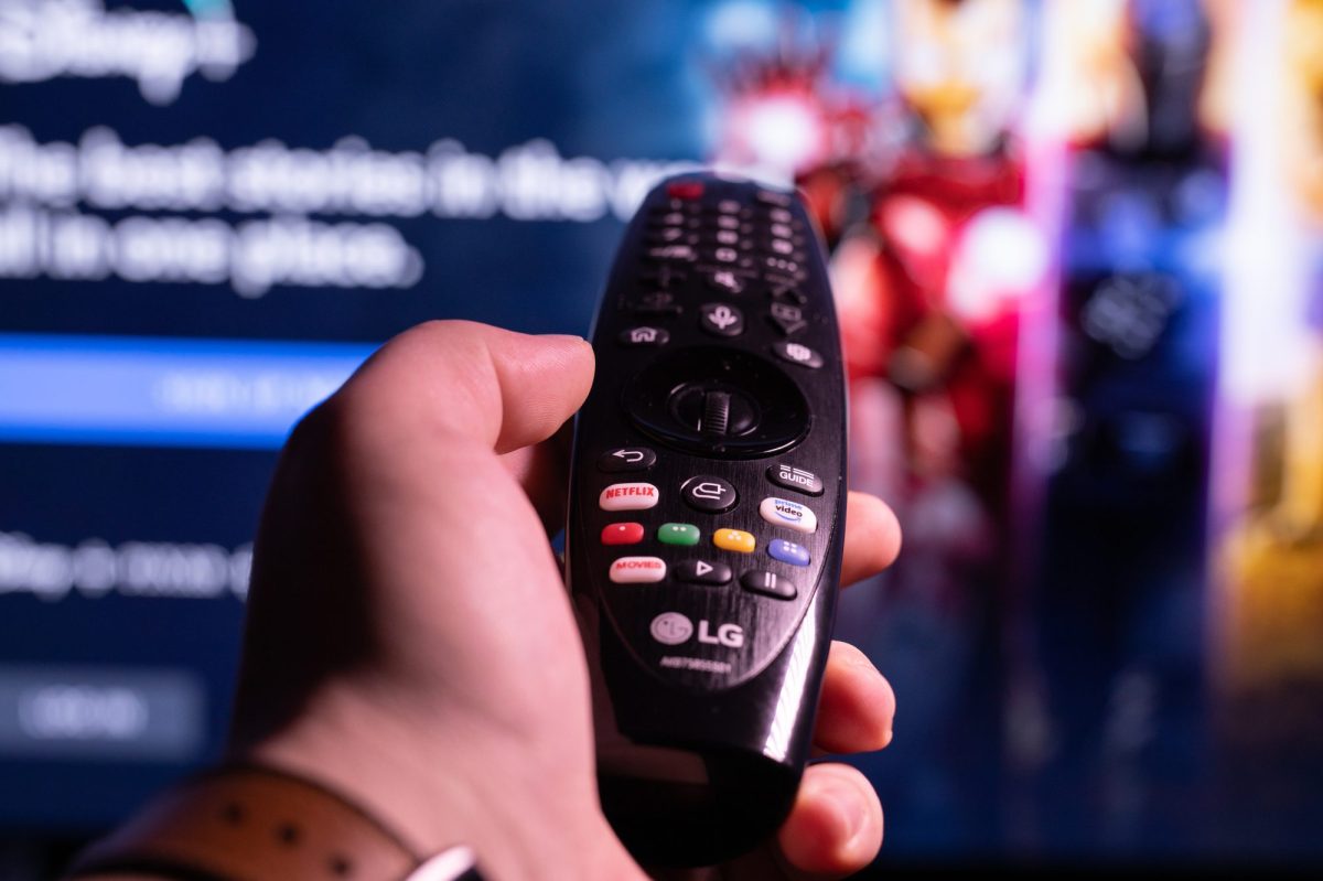 Person hält Fernbedienung in der Hand, die in Richtung eines Fernsehers zeigt.