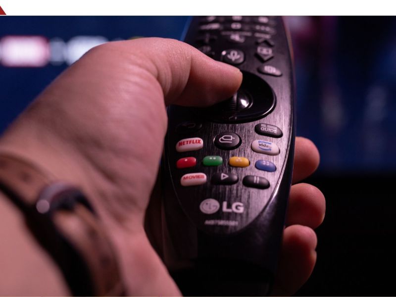Person hält eine LG-Fernbedienung in Richtung eines Fernsehers.