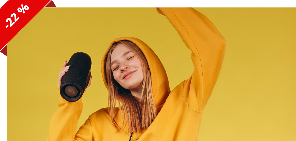 Eine Person im gelben Pullover hält einen Bluetooth-Lautsprecher in der Hand.