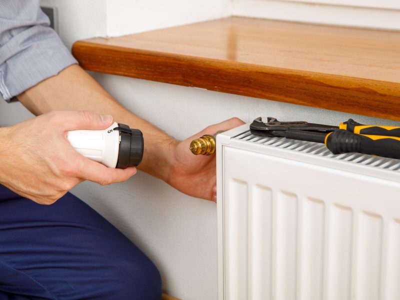 Ein Mann will ein Thermostat an der Heizung wechseln.
