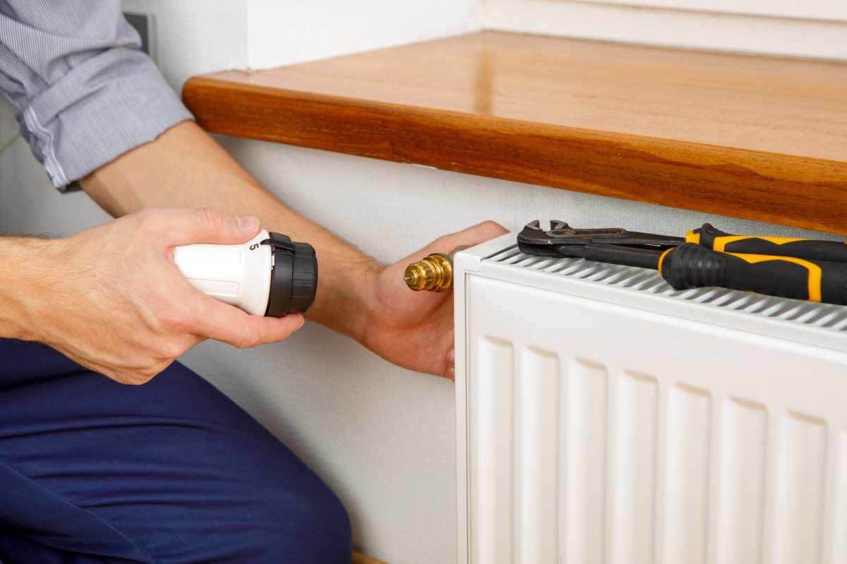 Ein Mann will ein Thermostat an der Heizung wechseln.