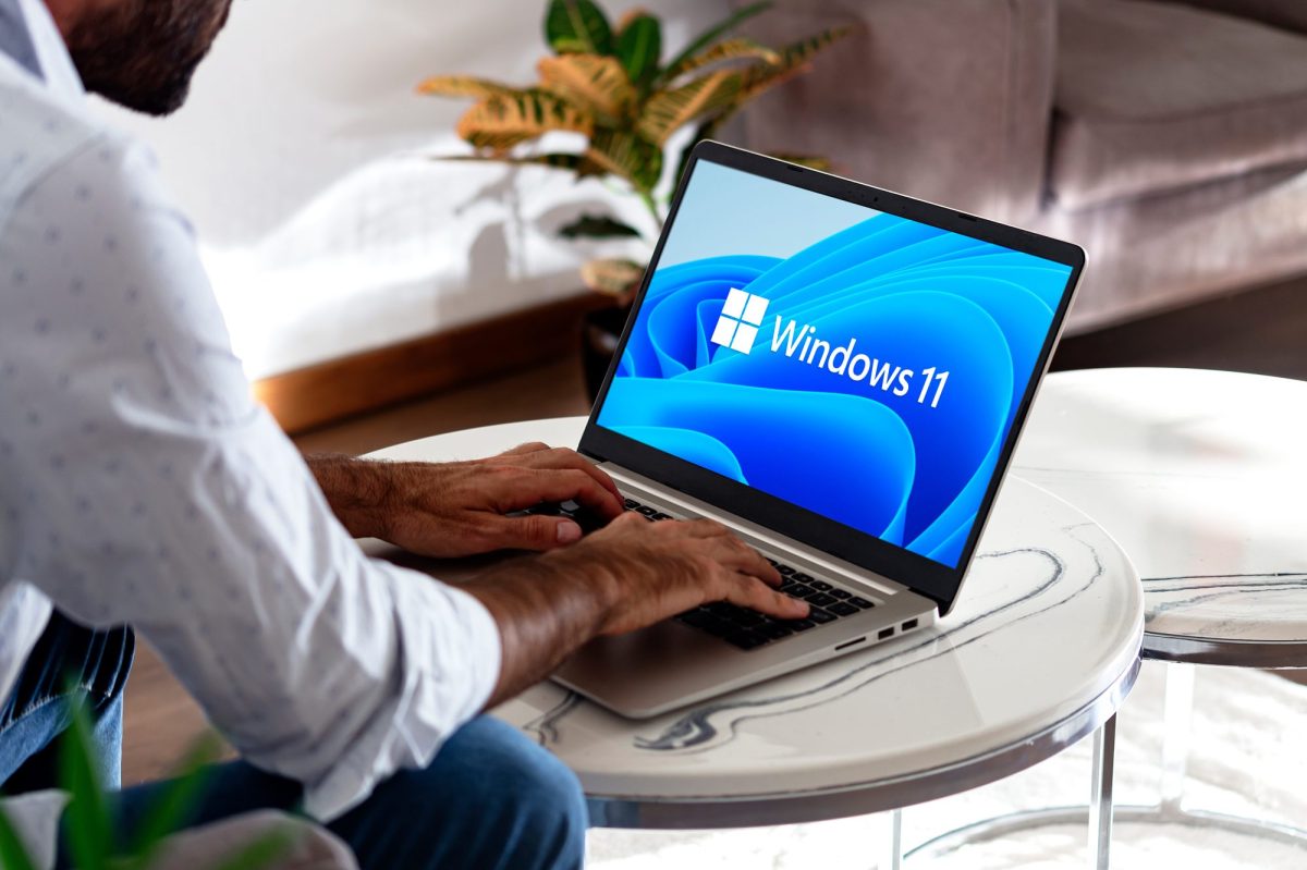 Person bedient einen Laptop, auf dessen Bildschirm, das Windows 11-Logo angezeigt wird.