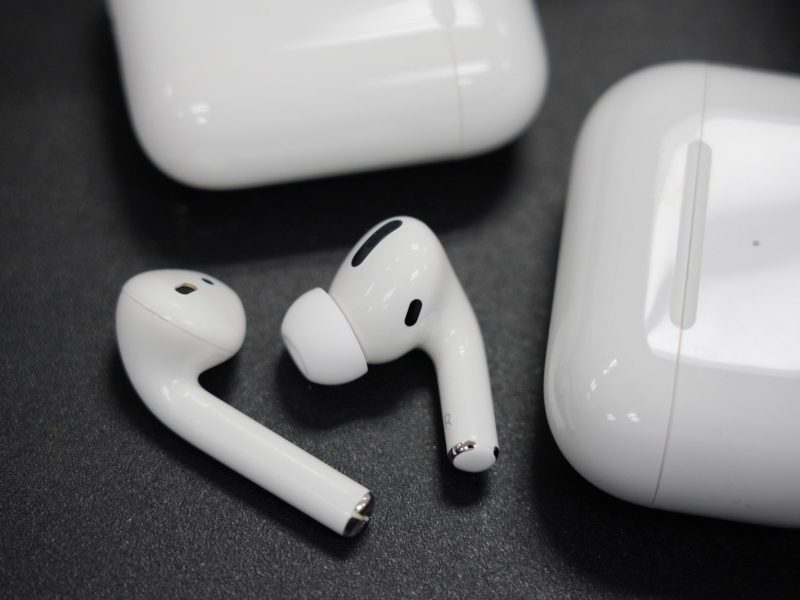 AirPods neben Lade-Case auf schwarzem Untergrund.