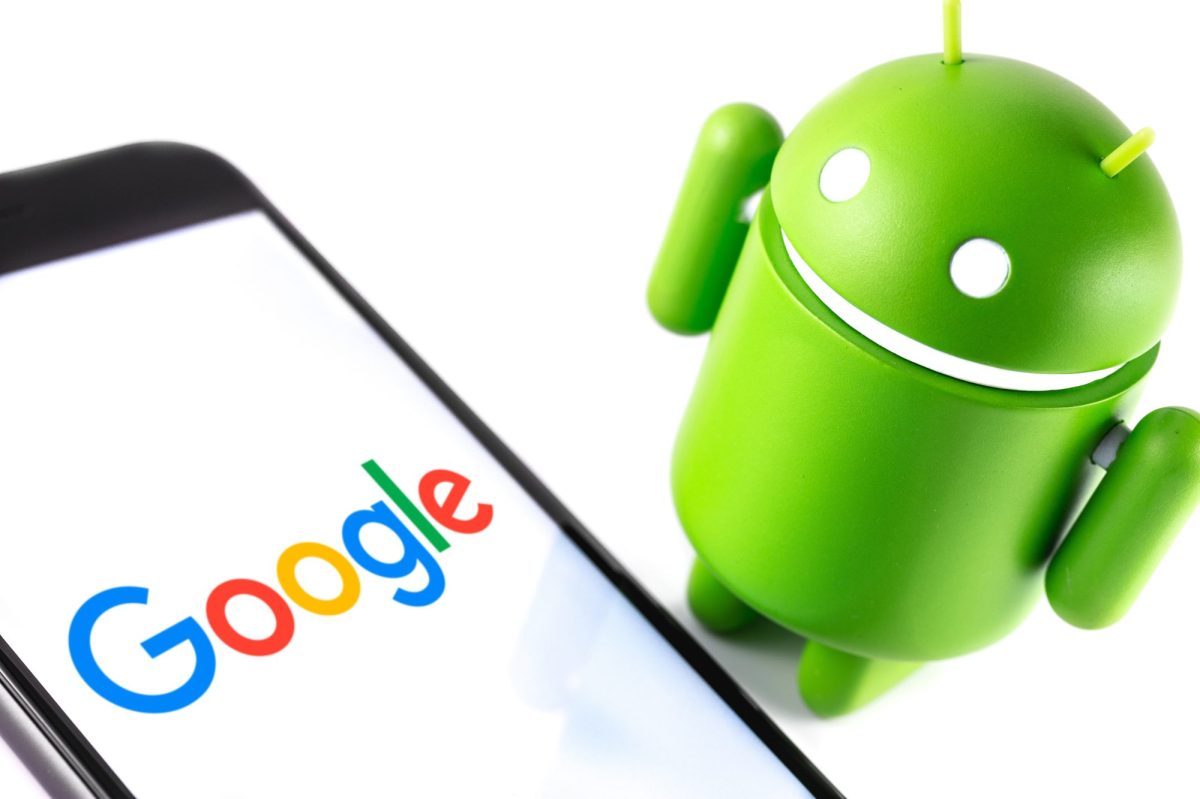 Android-Maskottchen steht neben einem Handy, auf dessen Bildschirm das Google-Logo zu sehen ist.