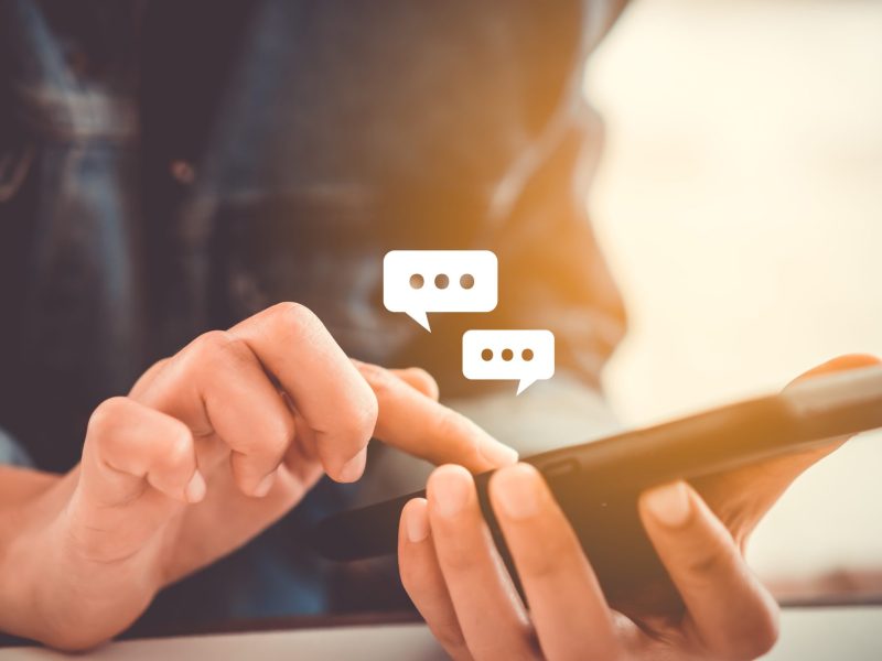 Eine Person hält ein Smartphone in der Hand. Darüber erscheinen Sprechblasen.