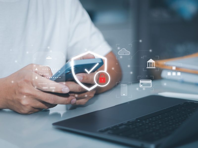 Person hält Handy in der Hand. Darüber liegen verschiedene Daten- und Sicherheitssymbole.