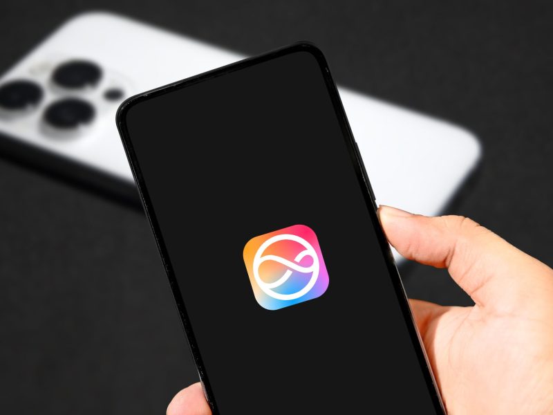Person hält ein iPhone in der Hand, auf dem Display ist das iOS-Logo zu sehen.