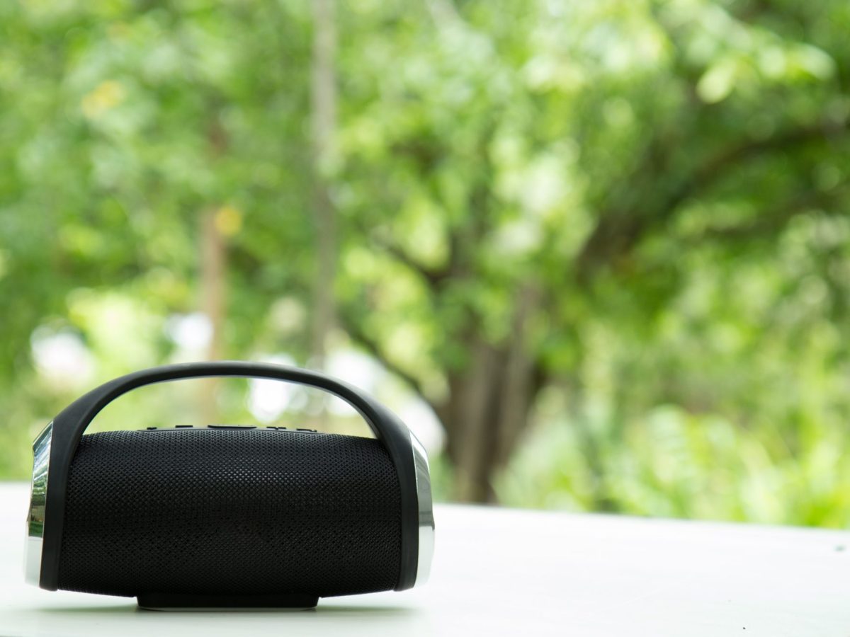 Bluetooth-Lautsprecher steht auf einem Tisch. Im Hintergrund sind Bäume zu sehen.