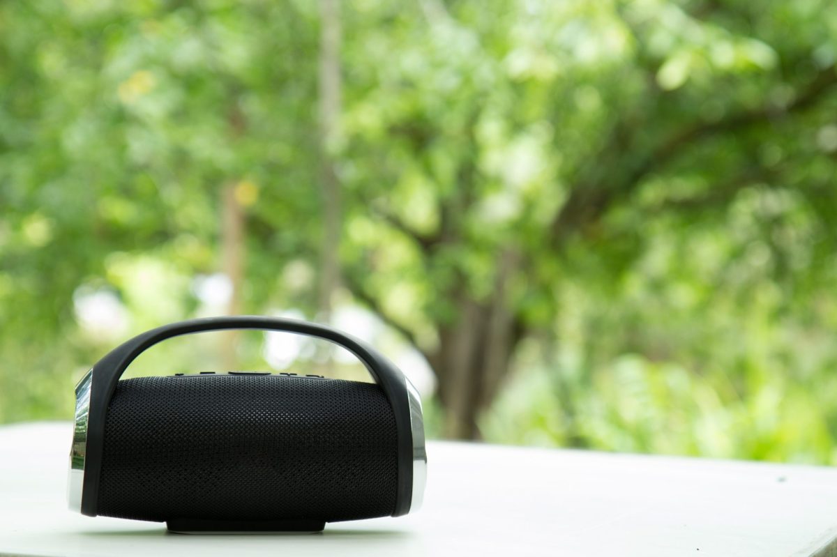 Bluetooth-Lautsprecher steht auf einem Tisch. Im Hintergrund sind BÃ¤ume zu sehen.