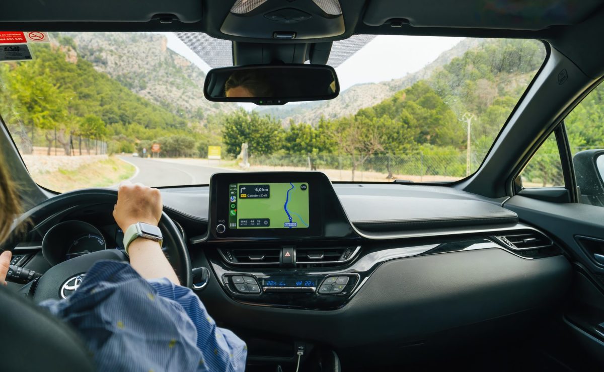 Person sitzt am Stuer eines Autos. Auf dem Fahrzeug-Display ist eine Navigations-App geöffnet.