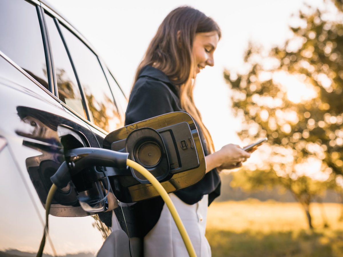 Frau lehnt an einem Elektroauto, das gerade lädt.