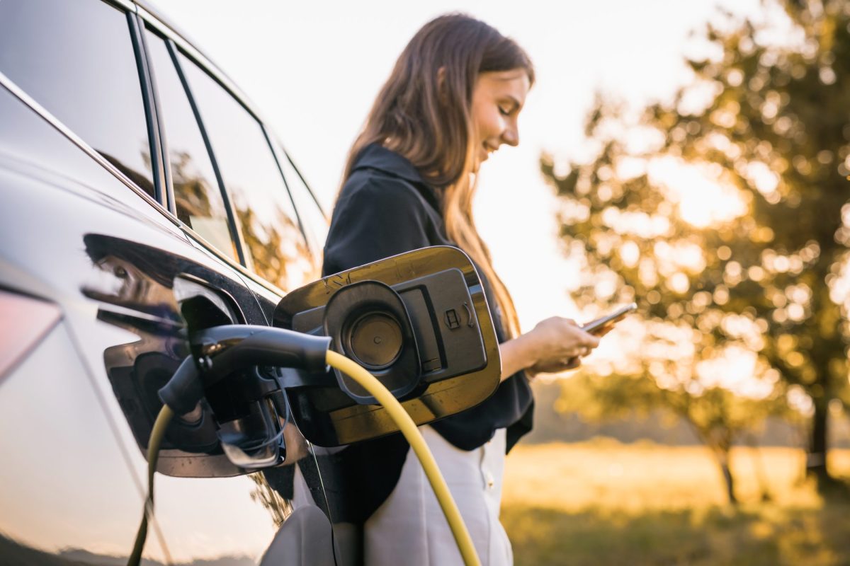 Frau lehnt an einem Elektroauto, das gerade lädt.