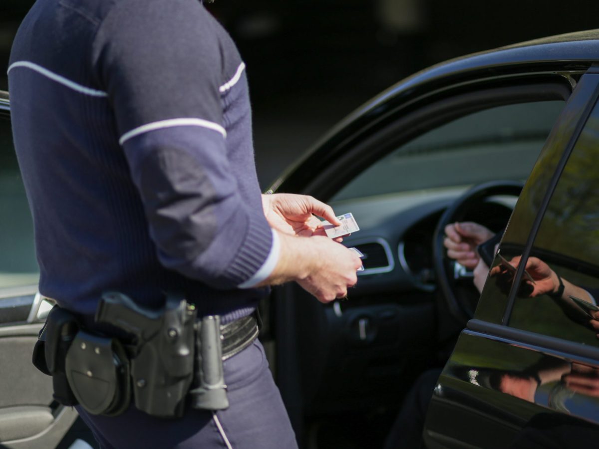 Polizist hält den Führerschein eines oder einer Fahrer*in in der Hand.