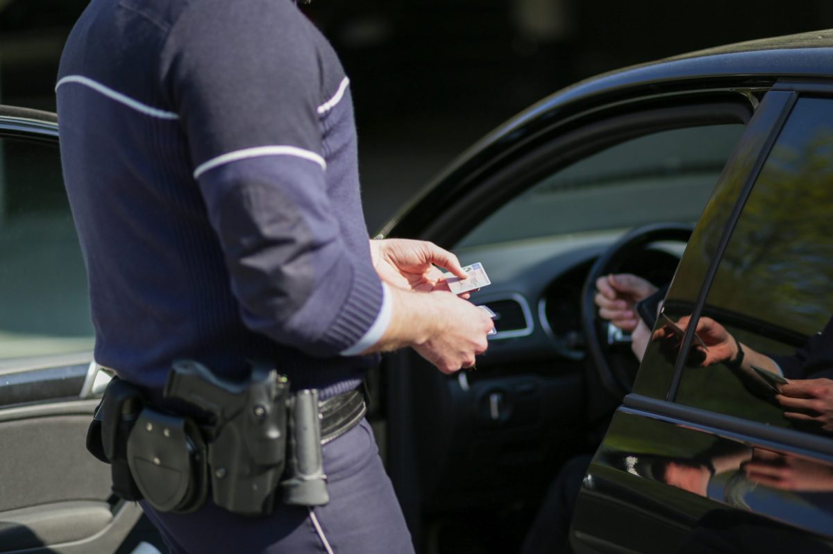 Polizist hält den Führerschein eines oder einer Fahrer*in in der Hand.