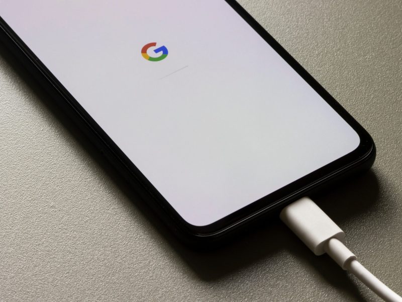Ein Smartphone ist an ein Ladekabel angeschlossen, auf dessen Display wird das Google-Logo angezeigt.