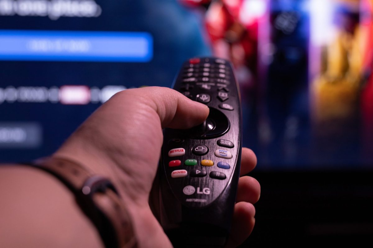 Person hält eine LG-Fernbedienung in der Hand und richtet sie auf einen Fernseher.