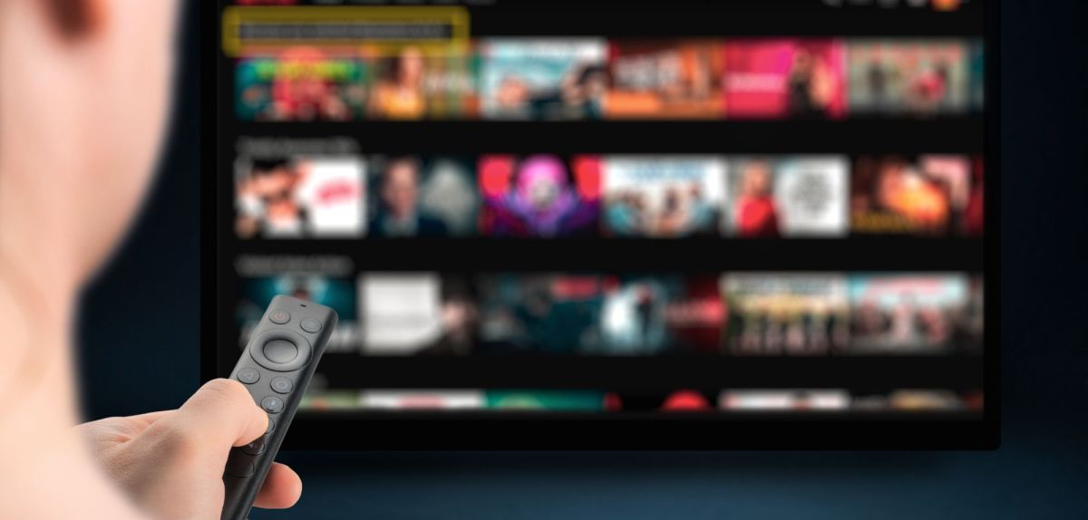 Person mit Fernbedienung vor einem Fernseher