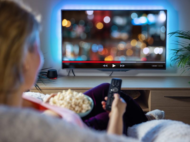 Person sitzt vor dem Fernseher, mit einer Schüssel voll Popcorn auf dem Schoß.