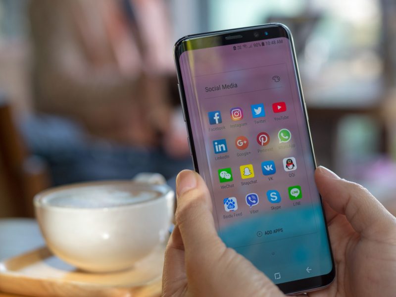Person hält ein Handy in der Hand, auf dessen Display mehrere Apps angezeigt werden.