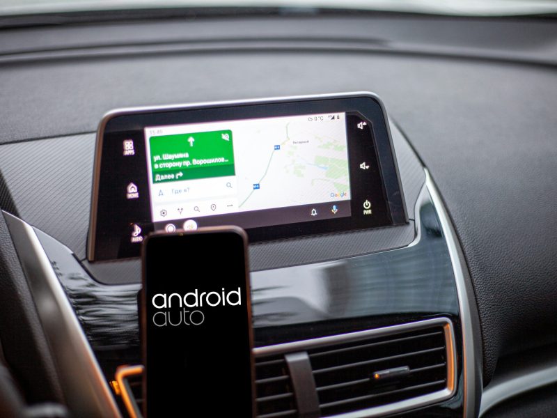 Android Auto auf einem Smartphone, im Hintergrund läuft ein Navi auf dem Fahrzeug-Display.