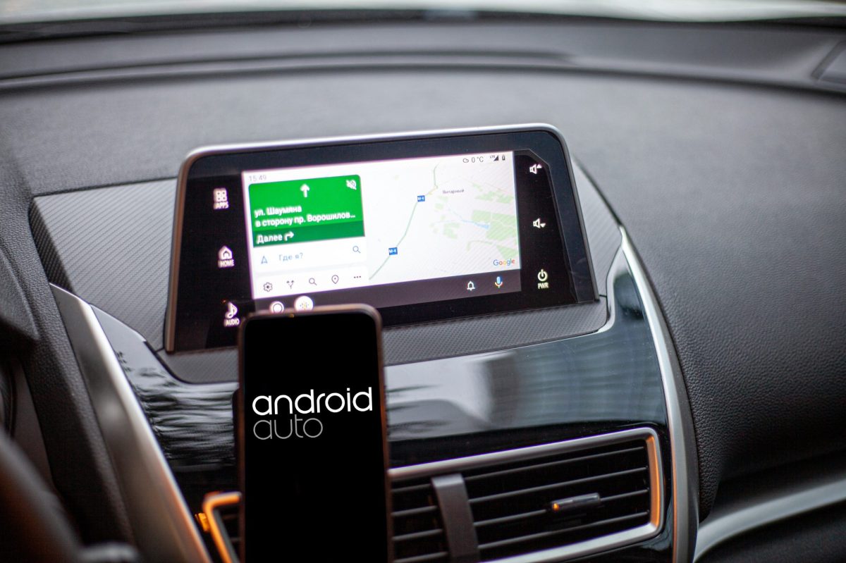 Android Auto auf einem Smartphone, im Hintergrund läuft ein Navi auf dem Fahrzeug-Display.