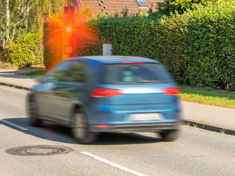 Ein fahrendes Auto wird von einer Radarfalle am Straßenrand geblitzt.