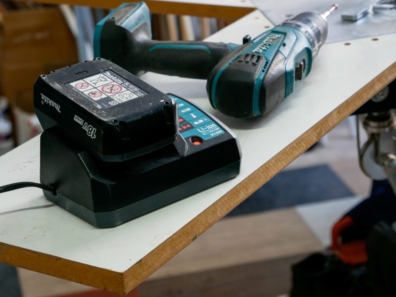 Makita-Akku liegt auf einem Ladegerät neben einem Akkuschrauber.