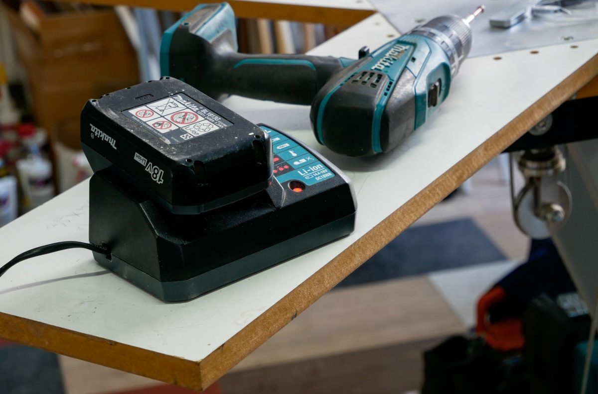 Makita-Akku liegt auf einem Ladegerät neben einem Akkuschrauber.